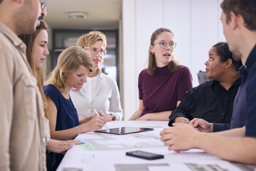 Mitarbeiter stehen gemeinsam am Tisch und besprechen Zeichenpläne