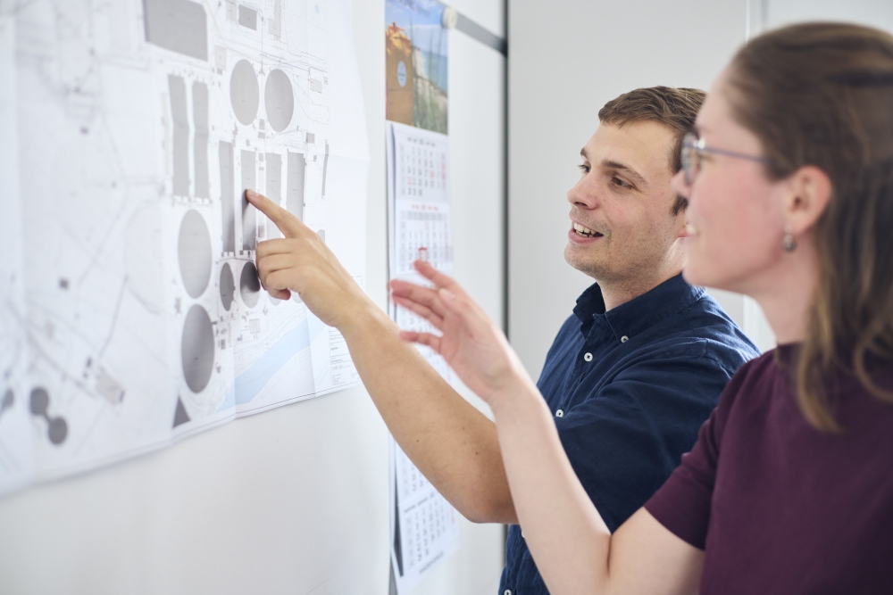 Zwei Mitarbeiter von Born Ermel besprechen eine Bauzeichnung, die an der Wand hängt