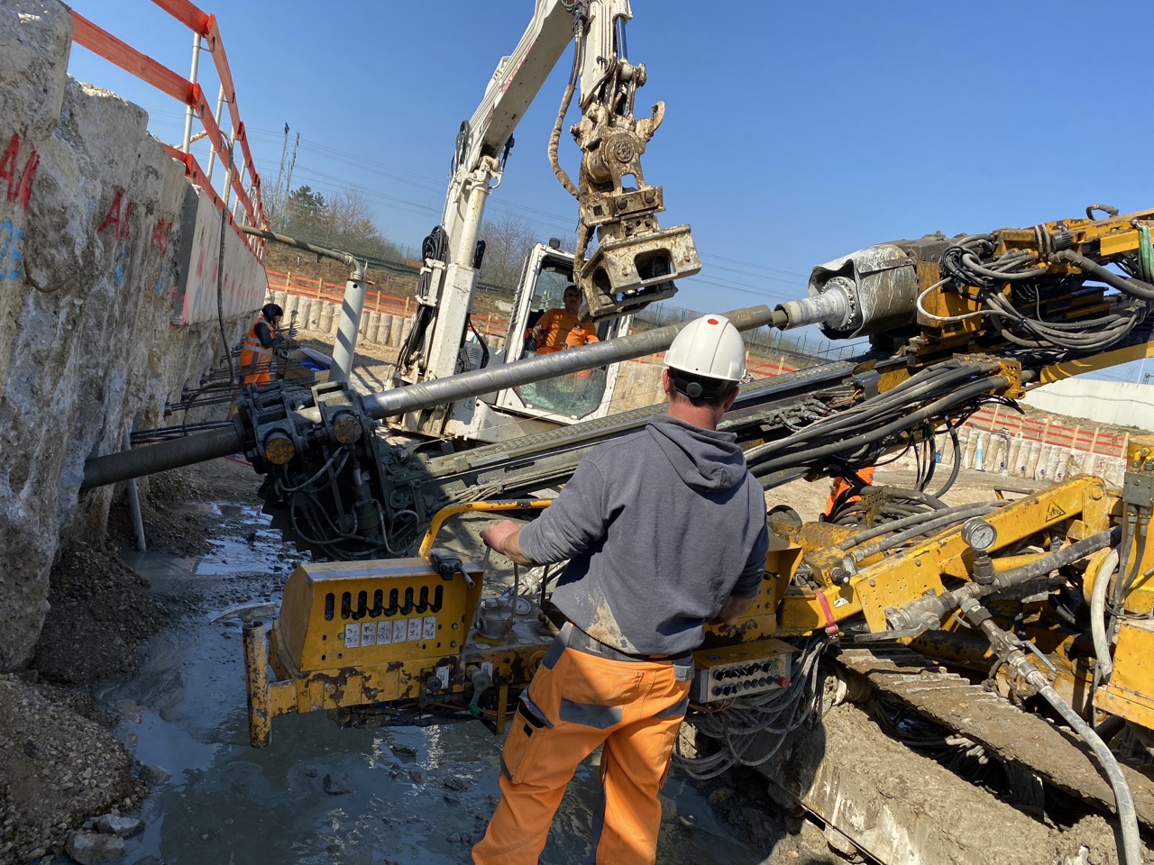 Bauarbeiten an einer Kläranlage. Bauarbeiter uund Bohrkran stehen in einer Grube