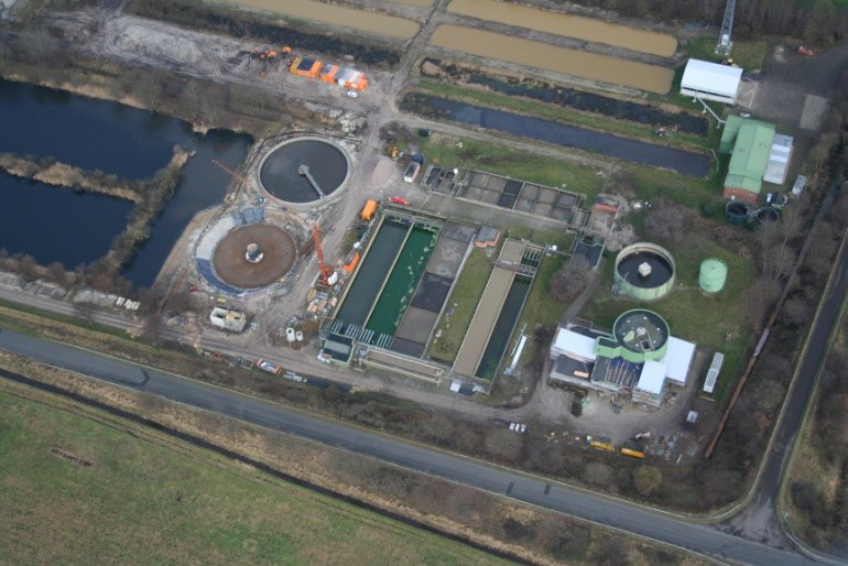 Luftaufnahme einer Kläranlage mit mehreren Becken, Rundklärern und Betriebsgebäuden im ländlichen Umfeld