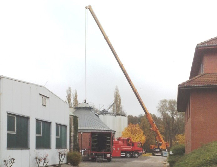 Kran hebt Bauteil an einem runden Anlagenbehälter auf dem Gelände einer Kläranlage während Montagearbeiten